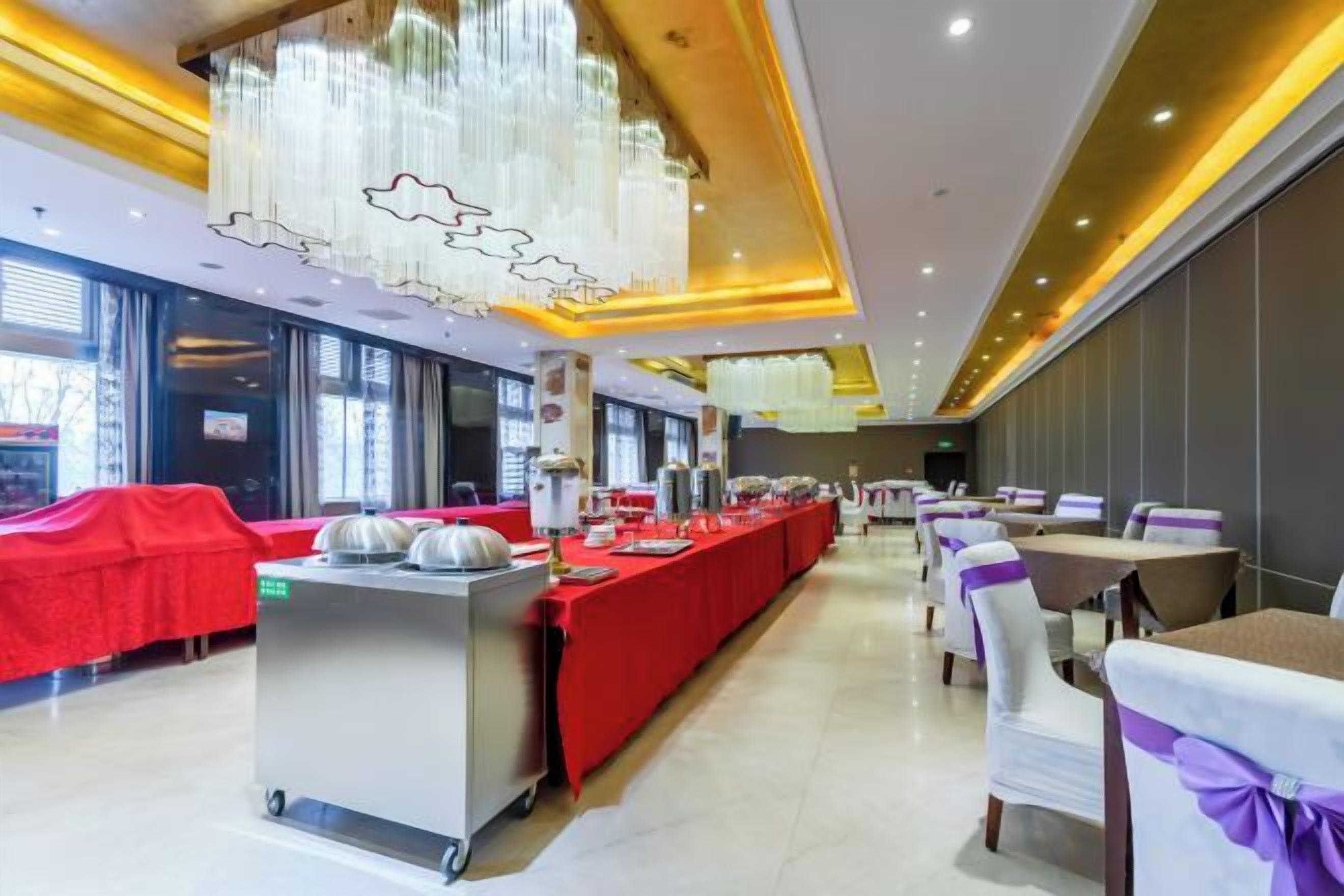 Une salle à manger d’hôtel avec une longue table dressée pour un banquet, un buffet et une rangée de tables individuelles avec des chaises.