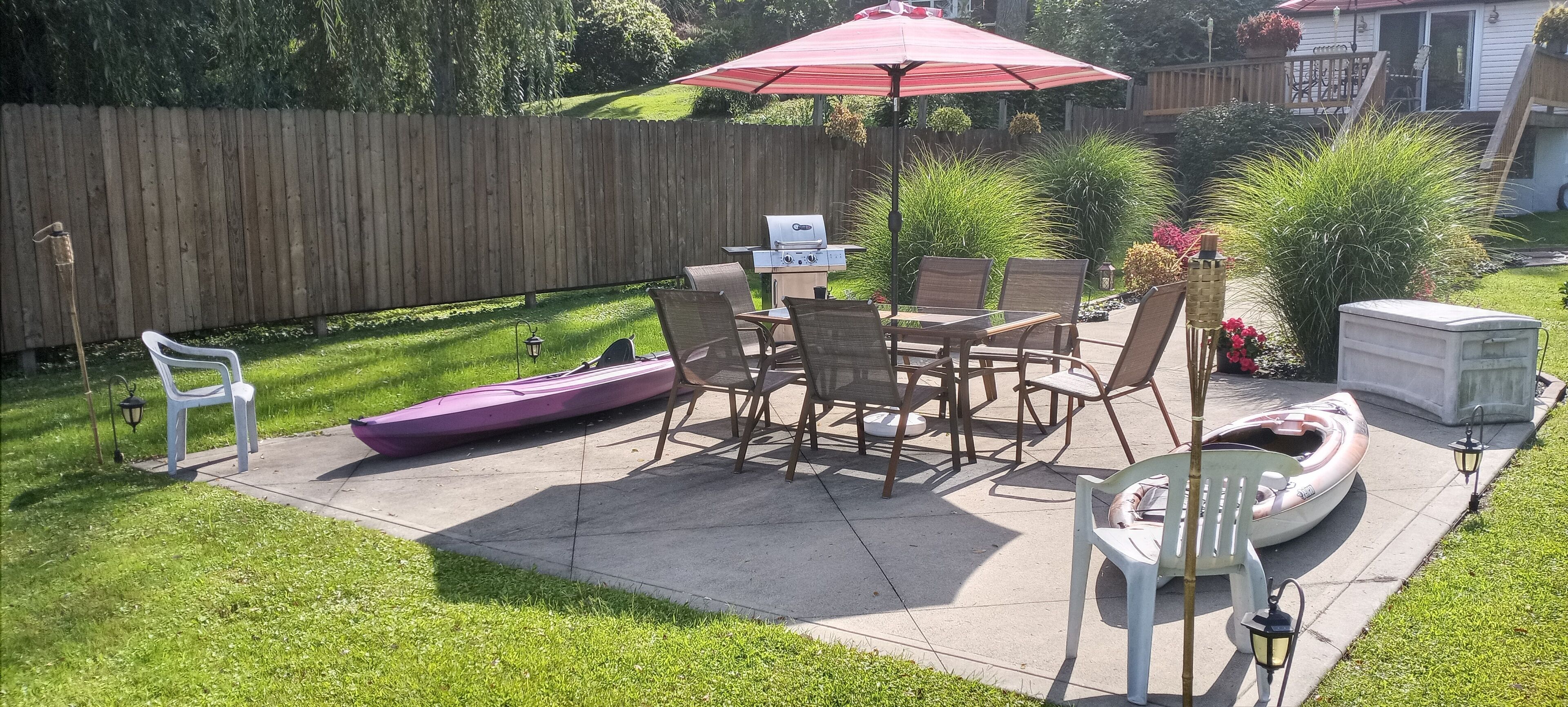 A backyard patio with a grill, chairs, and a table under a red umbrella.