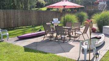 A backyard patio with a grill, chairs, and a table under a red umbrella.