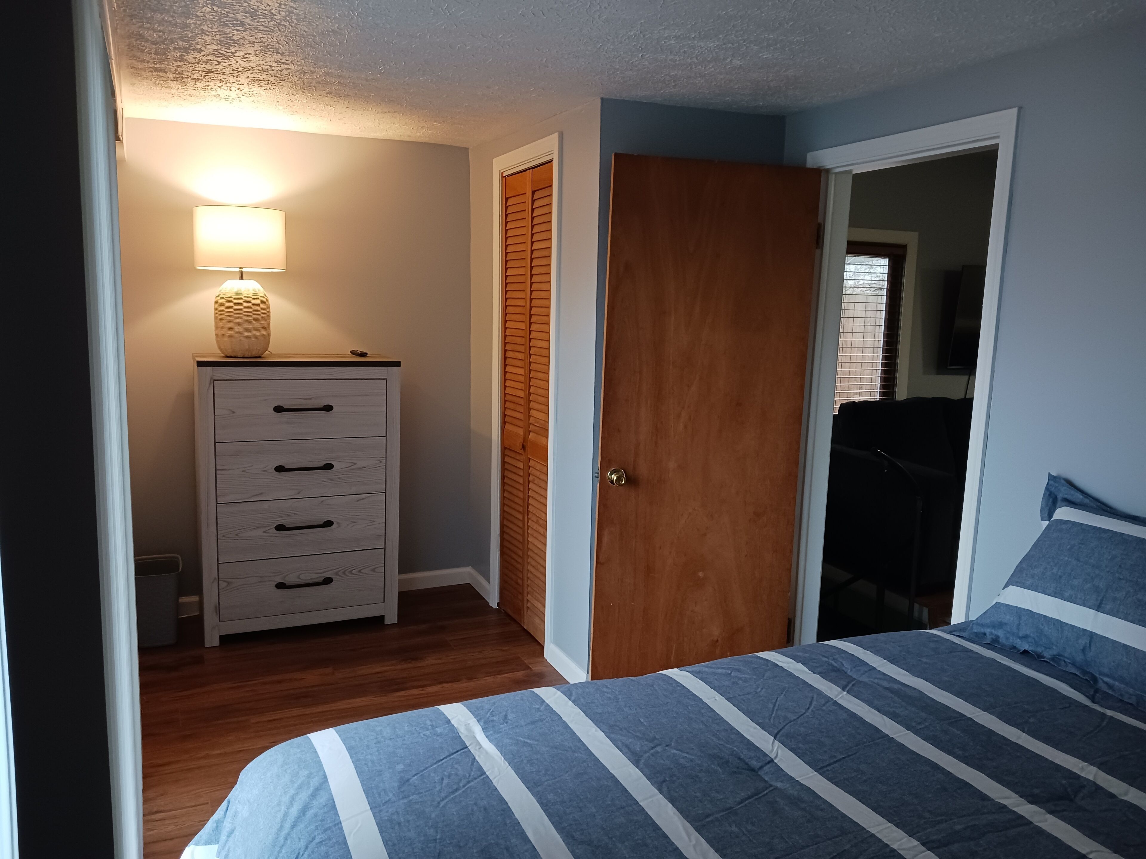 A bedroom with a bed, a dresser, a lamp, and a door.