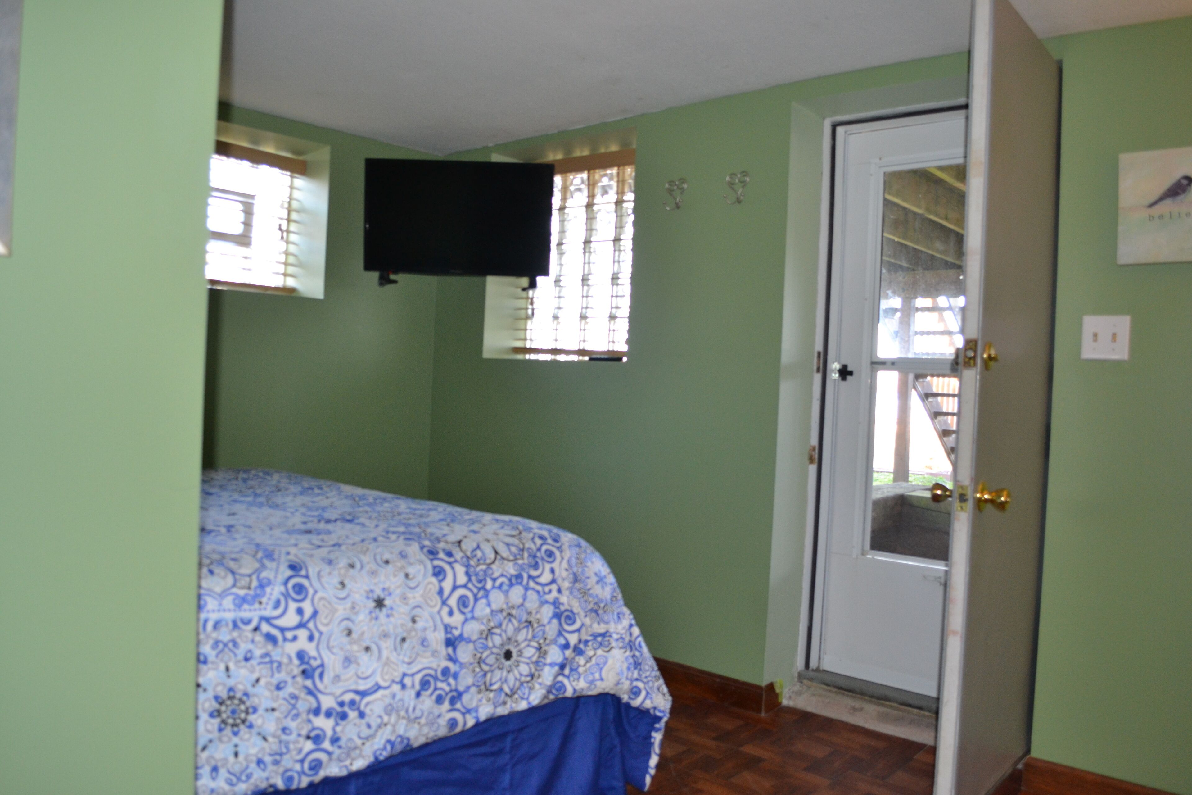 A room with a bed, a door, a window, and a wall-mounted television.