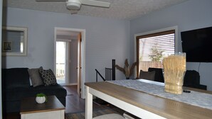 A living room with a ceiling fan, a sofa, a coffee table, a dining table, and a TV. - Akron (Portage Lakes) Peaceful Lakefront Cottage with Kayaks  (Akron)
