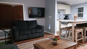 A living room with a dark sofa, a wooden coffee table, and a TV mounted on the wall. - Akron (Portage Lakes) Peaceful Lakefront Cottage with Kayaks  (Akron)