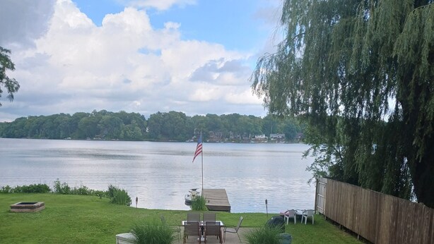 A wooden deck leading to a grassy area with a view of a lake and a dock. - Akron (Portage Lakes) Peaceful Lakefront Cottage with Kayaks  (Akron)
