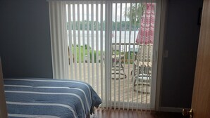 A bedroom with a bed, a wooden floor, a sliding glass door leading to an outdoor area with a patio and chairs. - Akron (Portage Lakes) Peaceful Lakefront Cottage with Kayaks  (Akron)