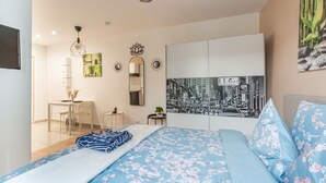 Un dormitorio con cama, escritorio, silla, espejo y un cuadro con vista urbana.