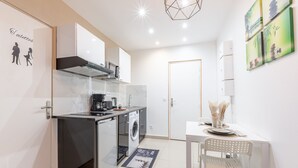 Cocina compacta con lavadora, cafetera y comedor con mesa y silla.