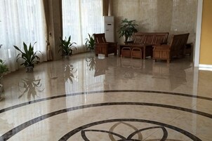 A lobby with a polished floor, a reception desk, and several potted plants.