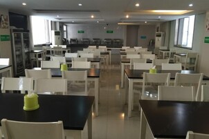 Un comedor amplio con varias mesas y sillas, un refrigerador y un ventanal que proporciona luz natural.