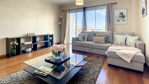 A modern living room with a sofa, a coffee table with a vase of flowers, a bookshelf, and a large window with curtains. - Charming Garajau by Atlantic Holiday (Santa Cruz)