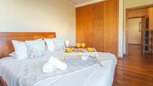 A neatly made bed with a tray of breakfast items, including croissants and orange juice, in a hotel room with wooden flooring and a large wardrobe. - Charming Garajau by Atlantic Holiday (Santa Cruz)