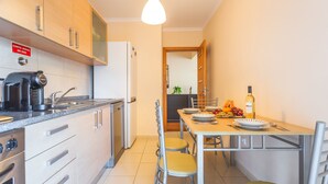 A modern kitchen with a dining area, equipped with stainless steel appliances and a dining table set for four. - Charming Garajau by Atlantic Holiday (Santa Cruz)
