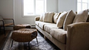Ett vardagsrum med en beige soffa, två fåtöljer i rotting, en mönstrad matta och en stol.