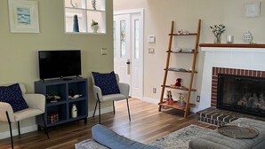A living room with a TV, sofas, a fireplace, and a wooden floor. - Townhouse Cottage on Oceanfront Property Adj. Samoset Golf Resort+Lighthouse (Rockport)