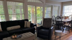 A living room with a black leather sofa, a grey ottoman, and a black leather chair. There is a dining table with chairs in the background. - Townhouse Cottage on Oceanfront Property Adj. Samoset Golf Resort+Lighthouse (Rockport)