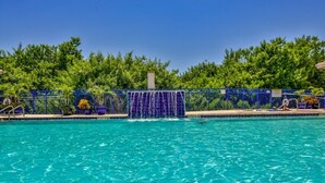 A swimming pool with a blue fence, surrounded by greenery. - Pet Family Friendly condo 2 heated pools, hot tub, sauna, bocce Tennis, etc (New Smyrna Beach)