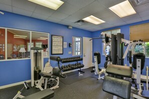 A gym with exercise equipment, a rack of dumbbells, and a door leading to another room.