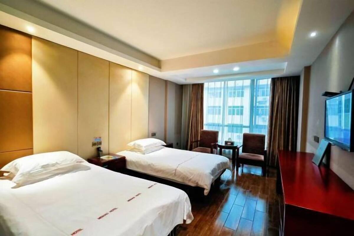 Ett hotellrum med två sängar, en TV, ett skrivbord och ett fönster med gardiner.
