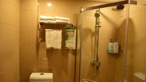 A glass-enclosed shower with a handheld showerhead and a glass shelf holding toiletries. - Meihao Boutique Hotel (Pingyang)