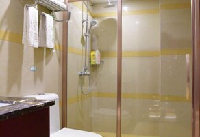 Zona de ducha con puerta de vidrio, perchero con toallas y estante pequeño con artículos de aseo.