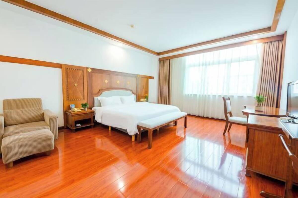A hotel room with a bed, a chair, a desk, and a large window.