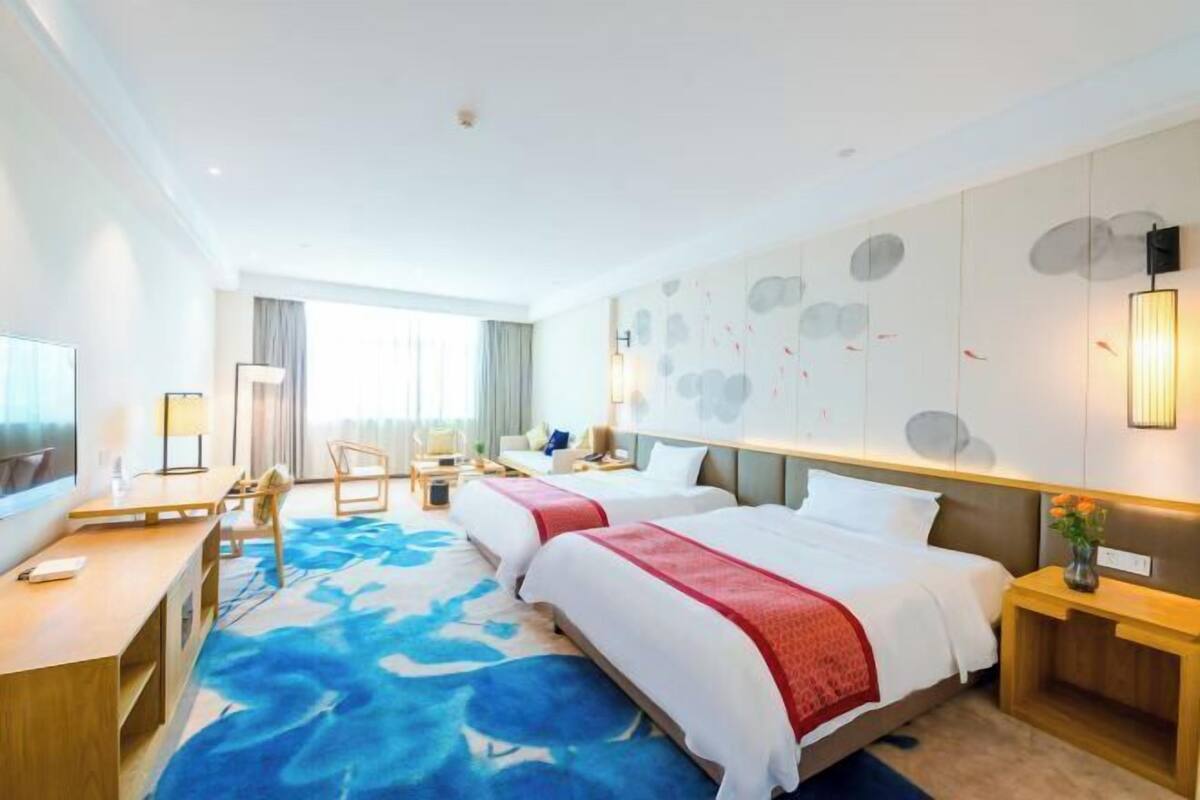 A hotel room with a large bed, a desk, a chair, a TV, and a wall with abstract art.