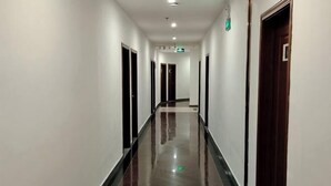 A long, narrow hallway with doors on both sides, a shiny tiled floor, and a green exit sign on the wall. - Hakkas Center Hotel (Meizhou)