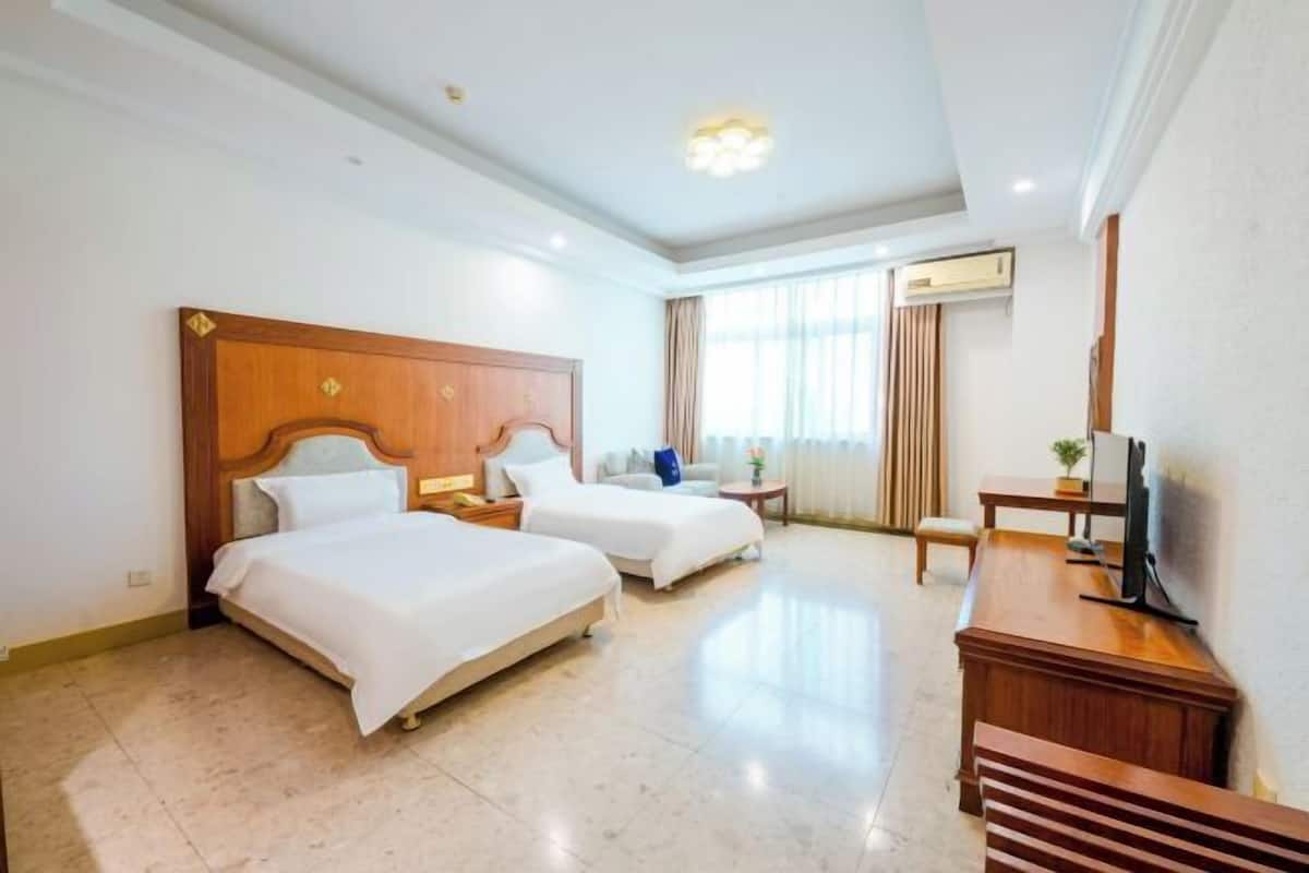 A hotel room with two beds, a desk, a TV, and a window with curtains.