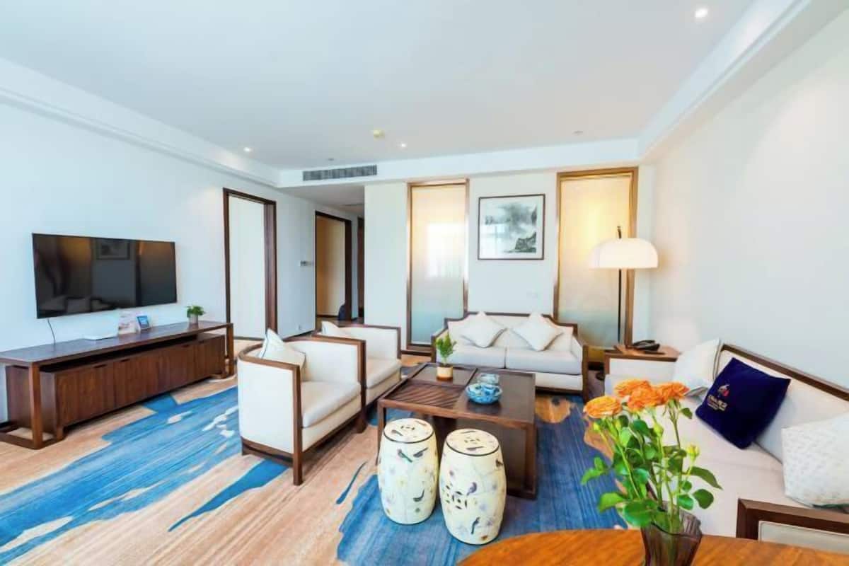 A modern hotel room with a flat-screen TV, a sofa, a coffee table, and a TV stand.