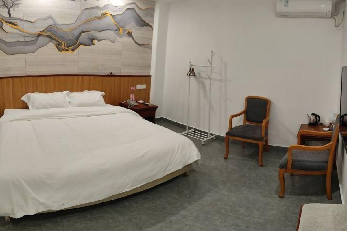 A hotel room with a large bed, two wooden chairs, a small table, and a wall-mounted air conditioner.