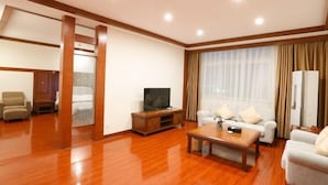 A spacious living room with a wooden floor, a sofa set, a coffee table, and a television. - Hakkas Center Hotel (Meizhou)