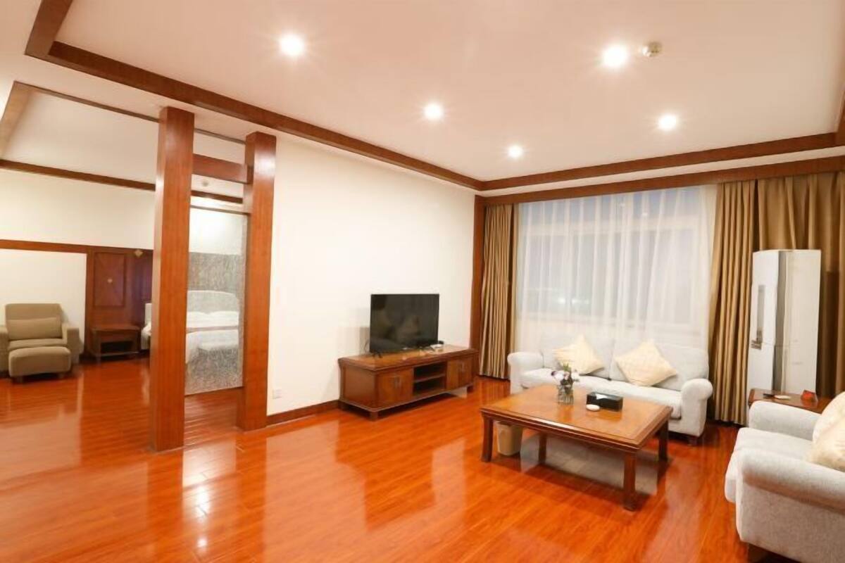 A spacious living room with a wooden floor, a sofa set, a coffee table, and a television.