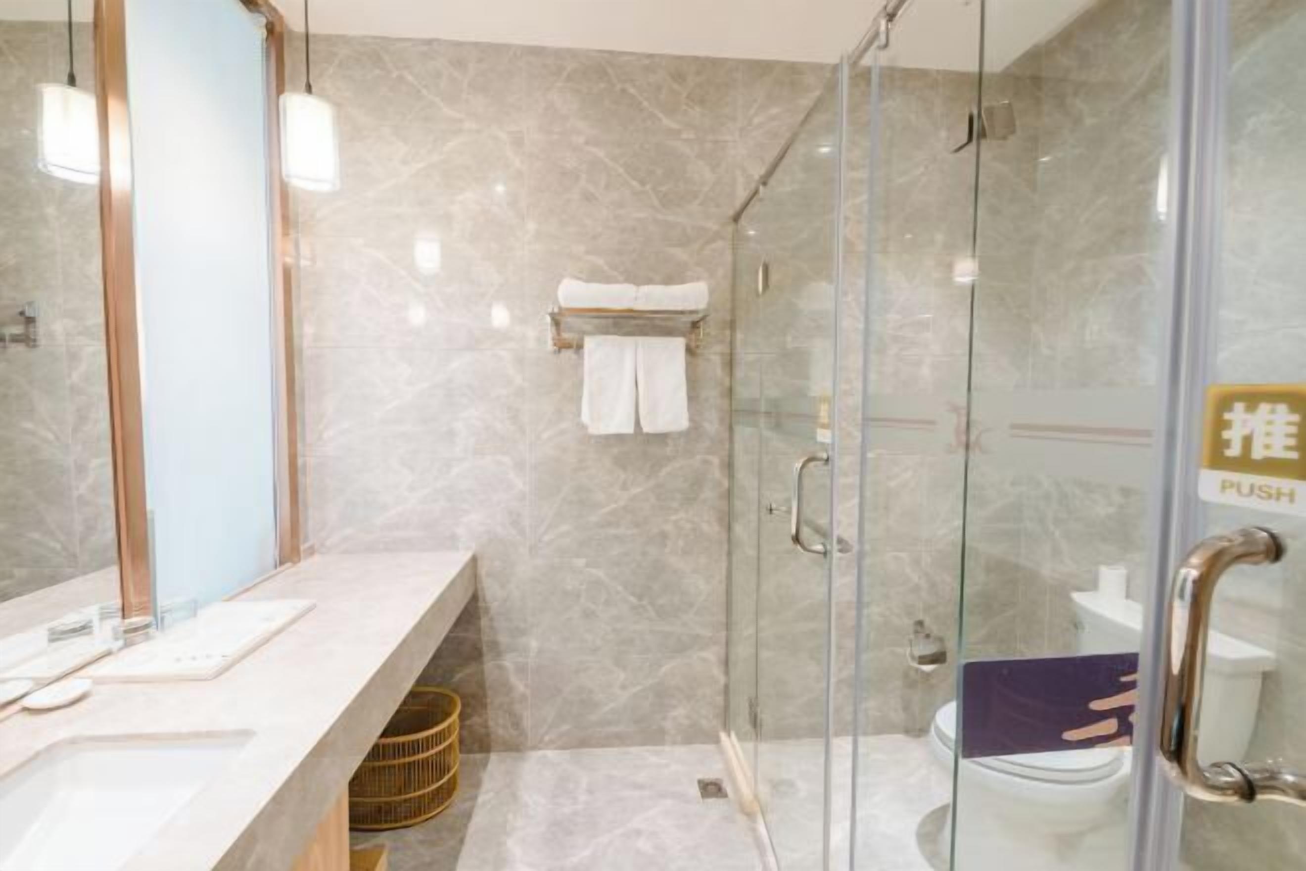 A modern bathroom with a glass-enclosed shower, a marble wall, a vanity with a mirror, and a towel rack.