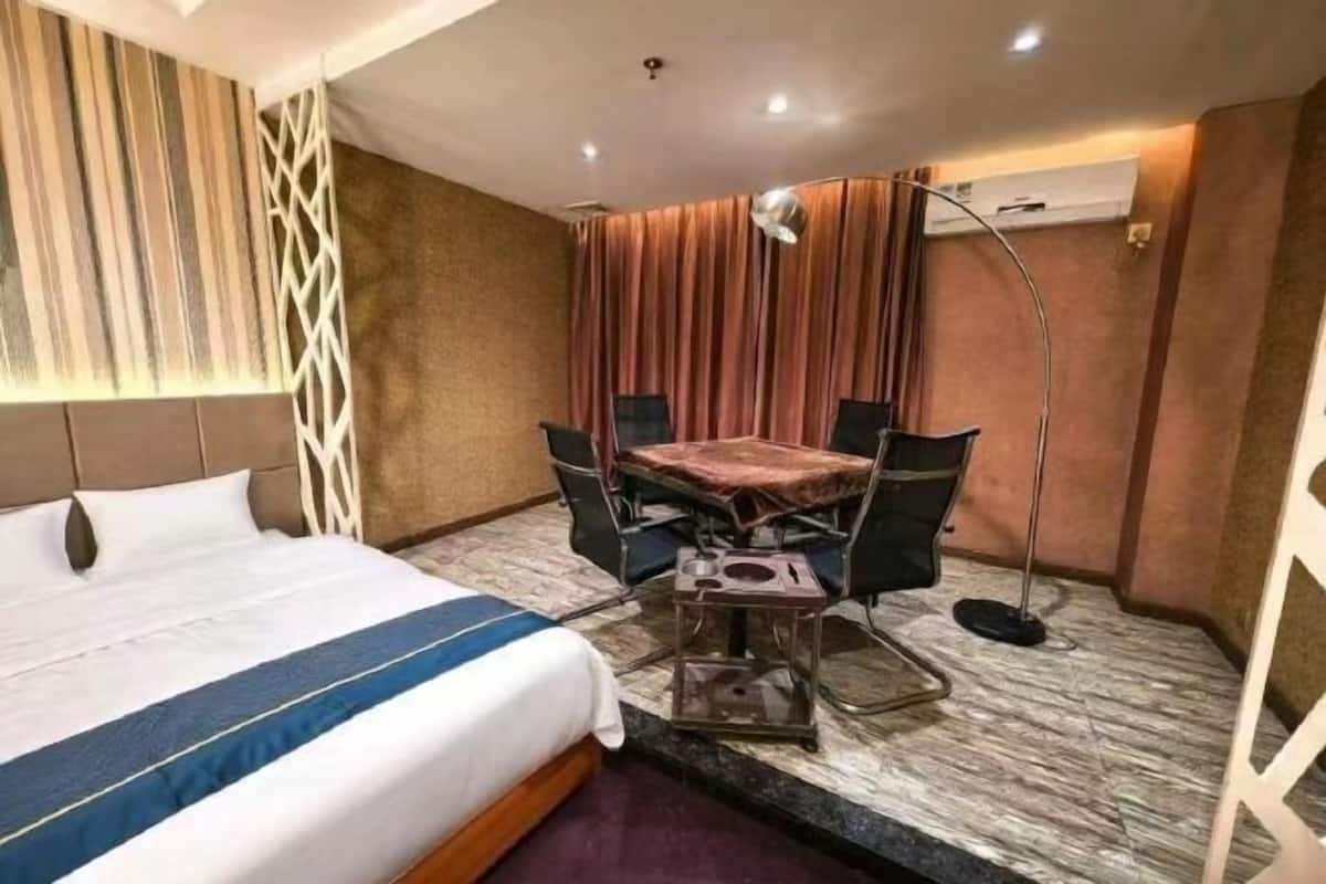 A hotel room with a bed, a desk with a chair, a lamp, and a curtain.
