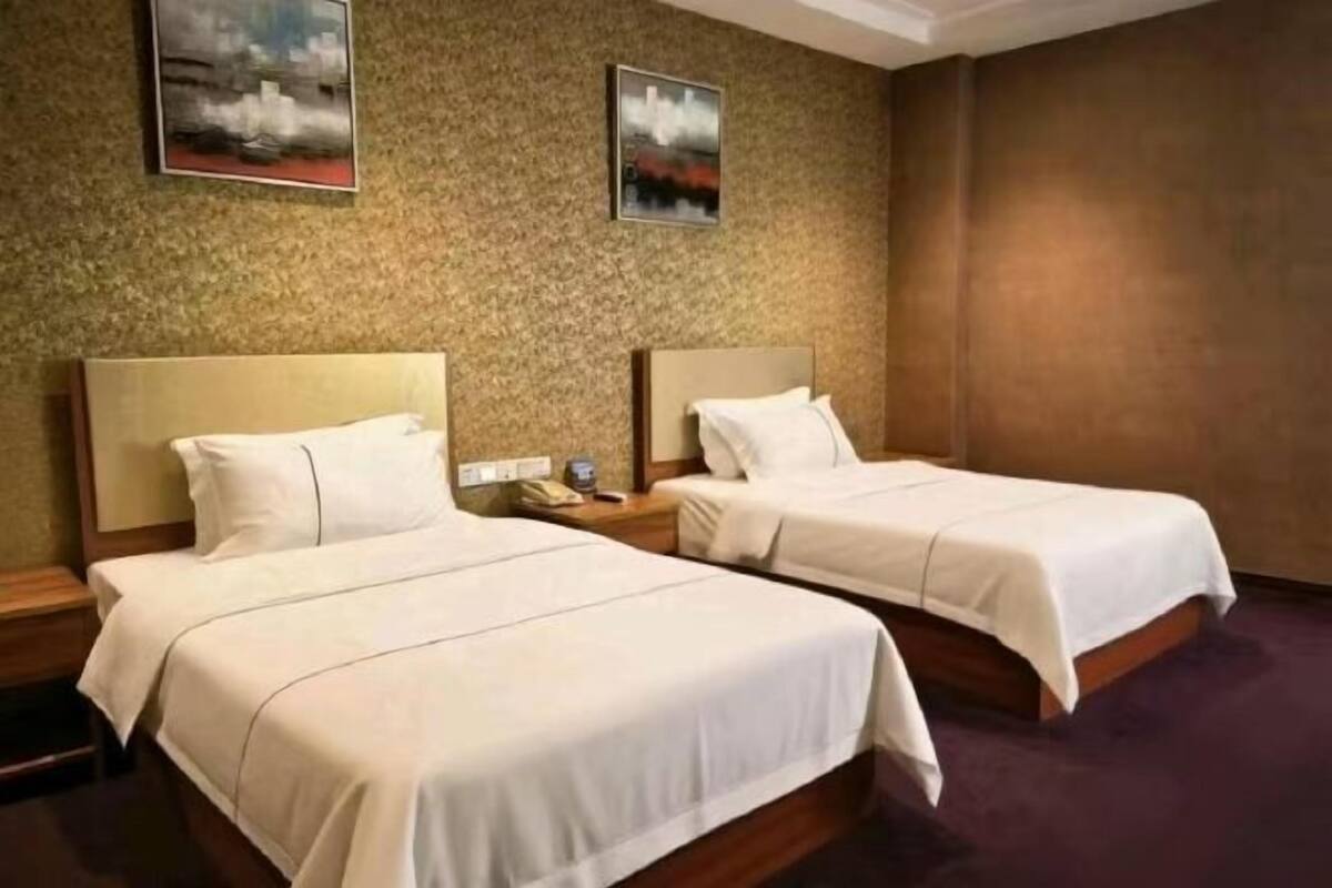 A hotel room with two single beds, a nightstand with a phone, and two framed pictures on the wall.