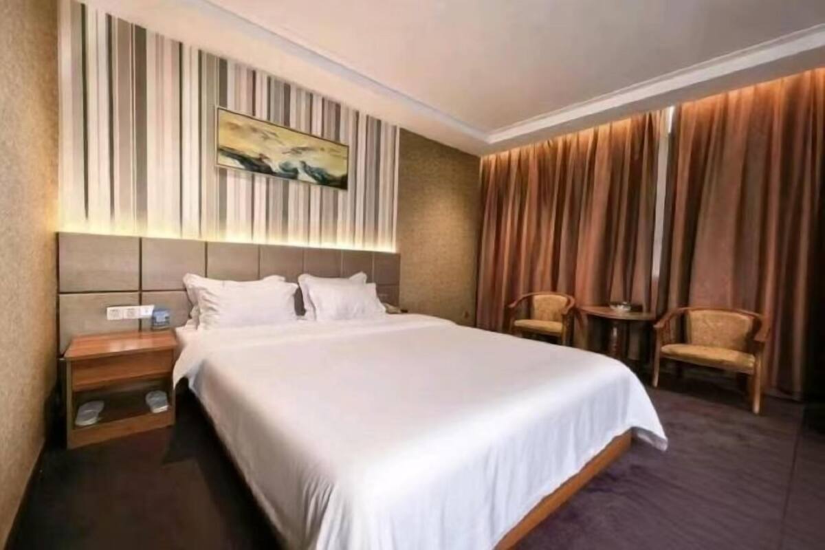 A hotel room with a large bed, a nightstand, a chair, a small table, and a painting on the wall.