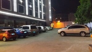 A parking lot with several cars parked in front of a building with illuminated windows. - Dingrun Business Hotel (Huizhou)
