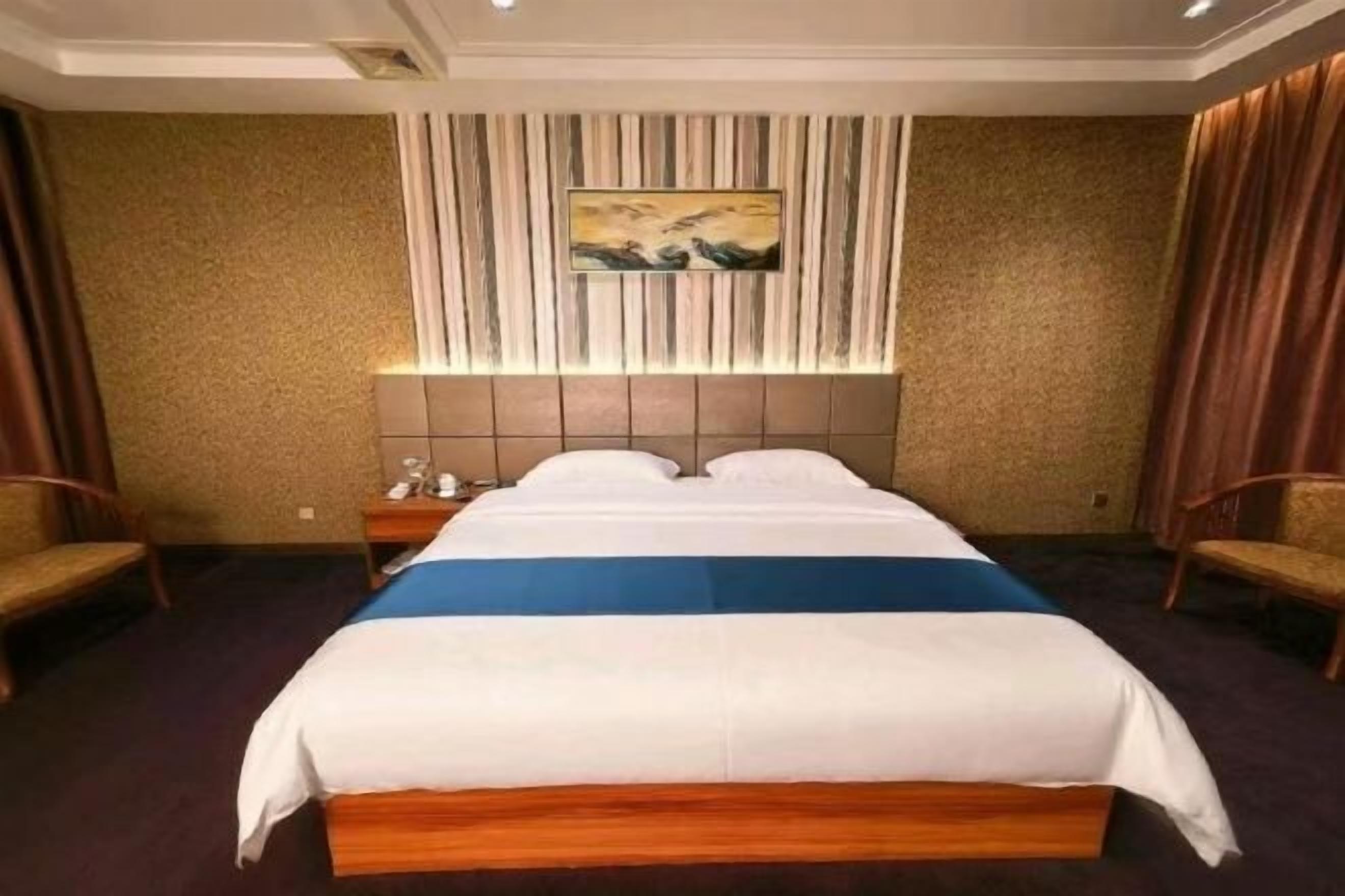 Ein Hotelzimmer mit einem großen Bett, einem Bettkopfteil mit einem Gemälde, einem Nachttisch und zwei Stühlen.