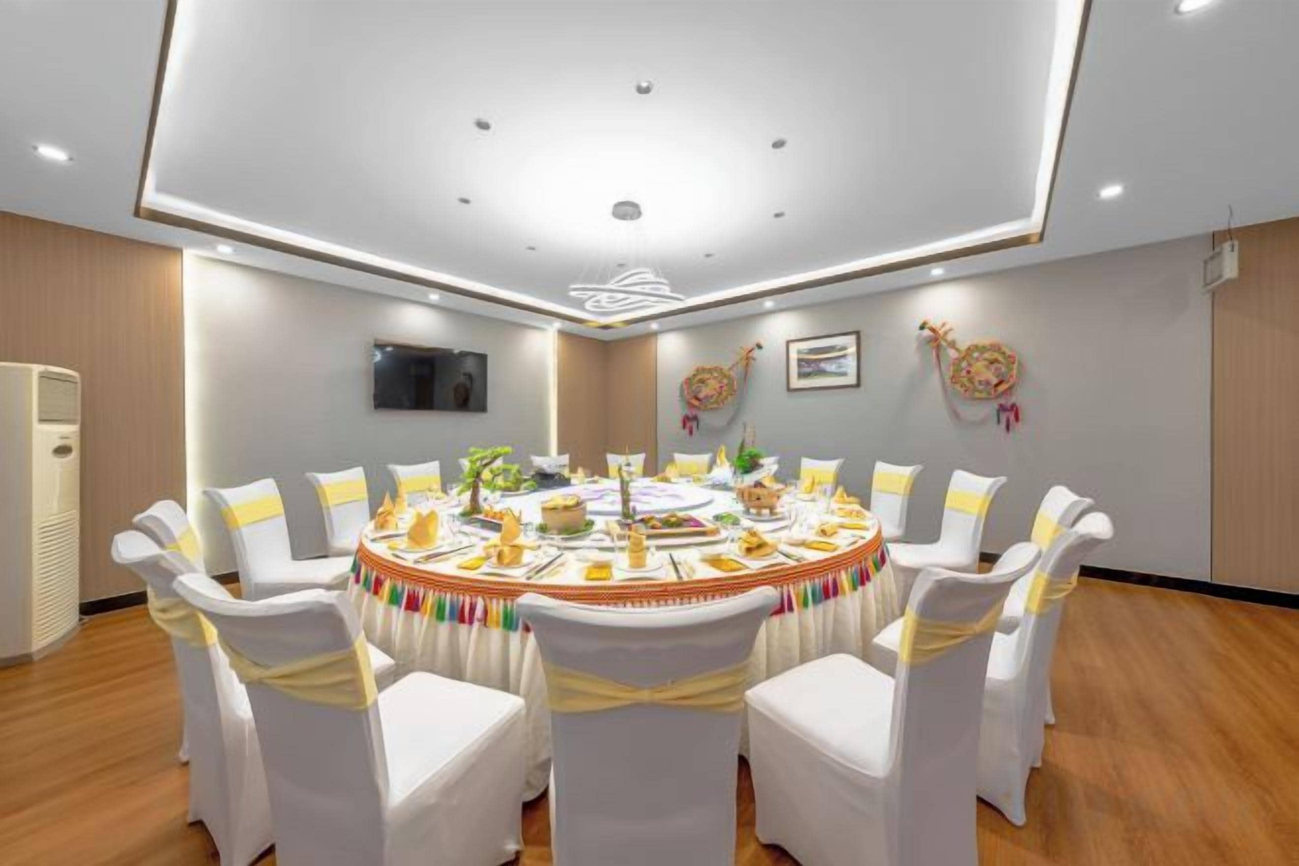 A conference room with a round table, white chairs with yellow sashes, and a flat-screen TV on the wall.