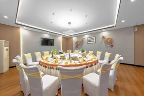 Un salón de conferencias con una mesa redonda, sillas blancas con cintas amarillas y un televisor de pantalla plana en la pared.