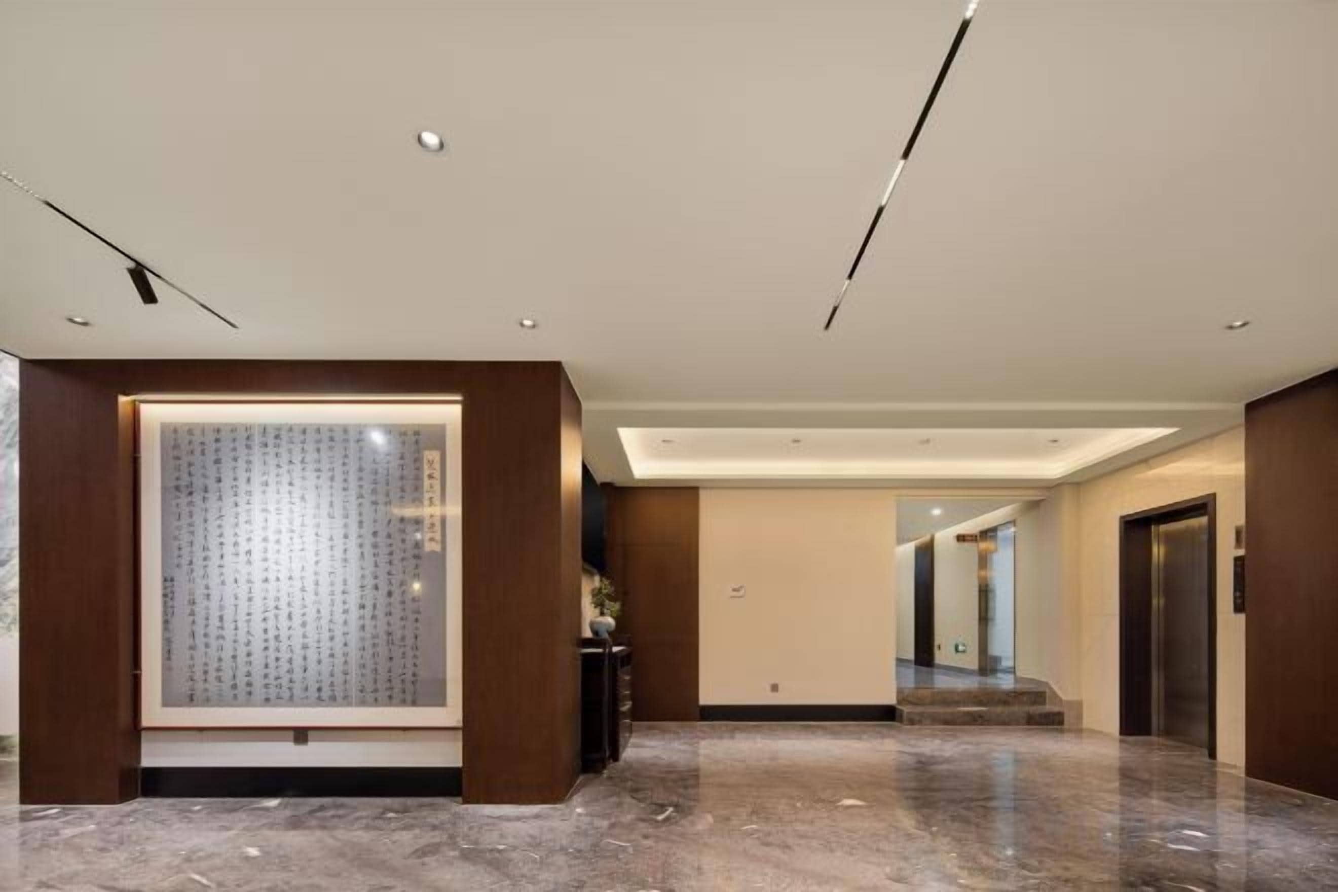 A modern hotel lobby with a marble floor, a large framed artwork, and a reception desk.
