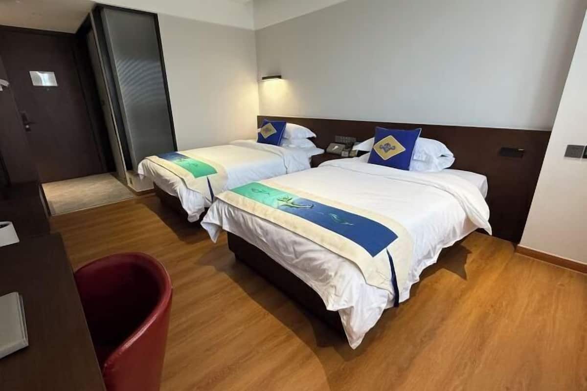 Habitación de hotel con dos camas, un escritorio y un cubo de basura rojo.