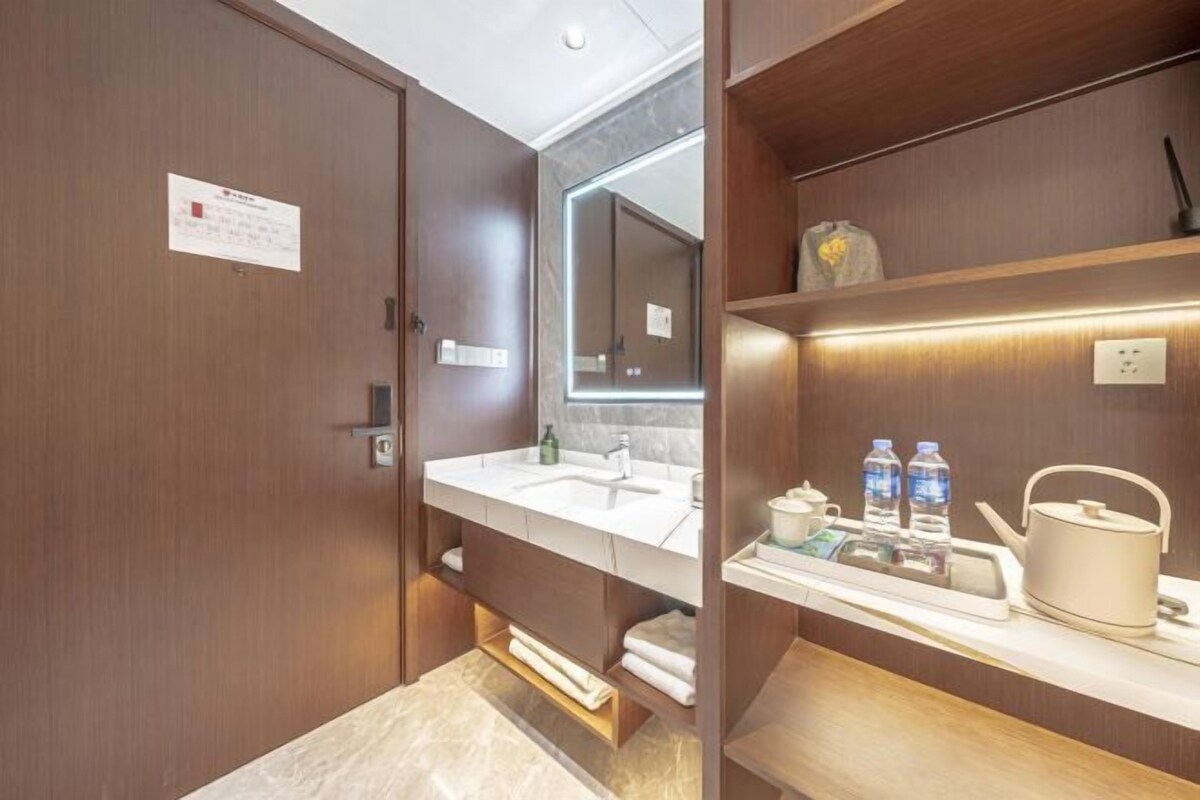 A modern bathroom with a large mirror, a sink, and a shelf with toiletries.
