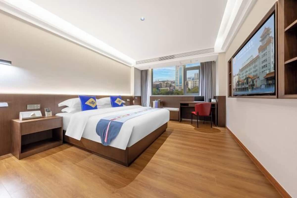 Habitación de hotel con cama, mesita de noche, escritorio, silla y una ventana grande con vista a la ciudad.
