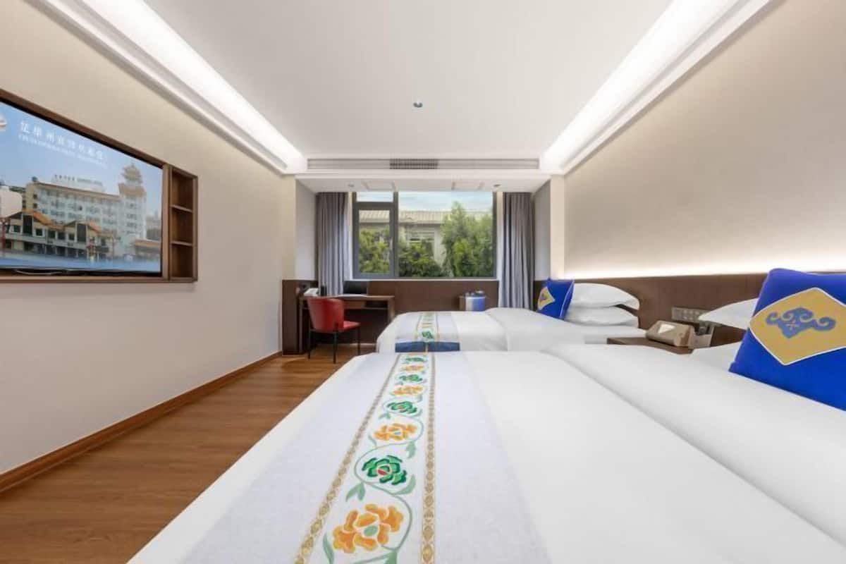 Una habitación de hotel con cama, escritorio, silla, televisor y ventana con cortinas.