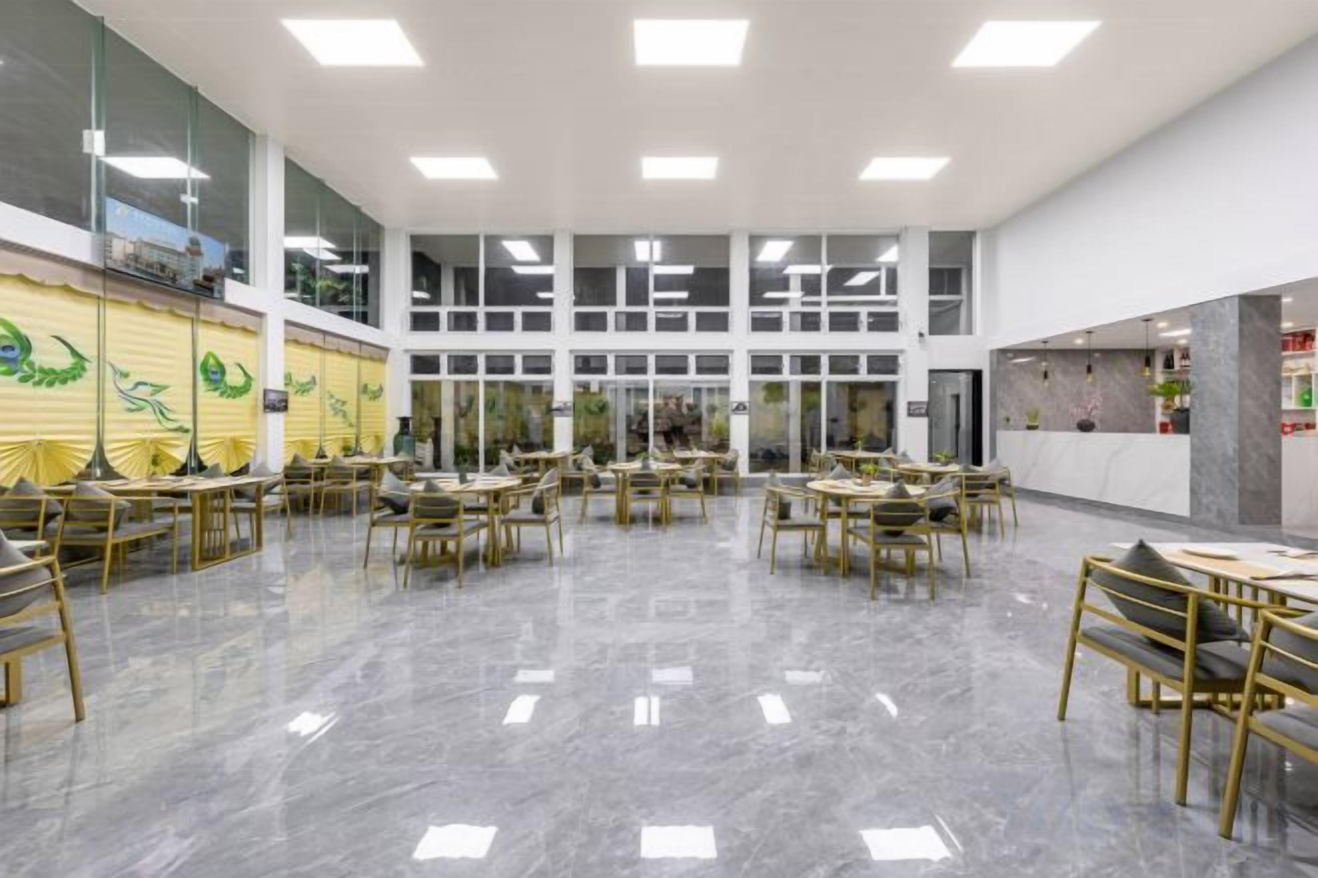 A spacious indoor area with multiple tables and chairs arranged in a circular pattern, large windows, and a high ceiling.