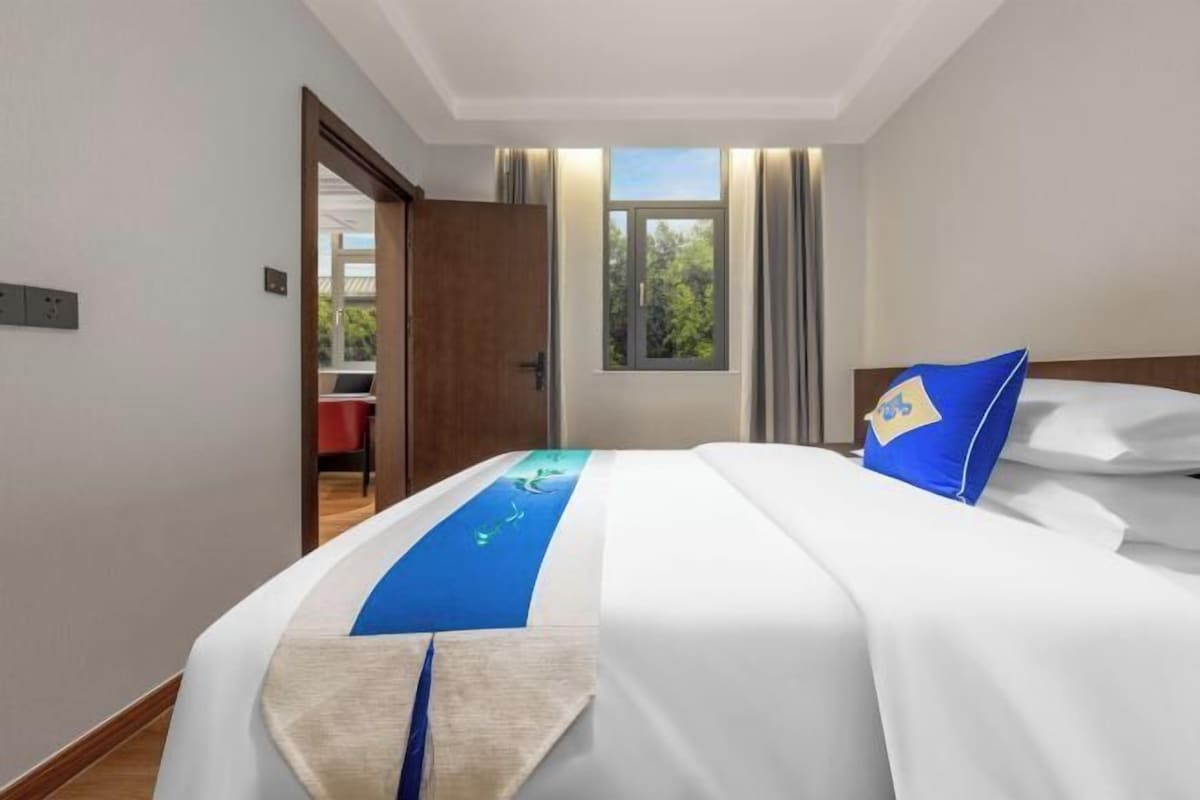 A hotel room with a bed, a window, and a door leading to another room.