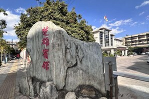A large rock with carved text, a building with a flag, and a clear sky. - Chuxiongzhou Hotel (Chuxiong City)
