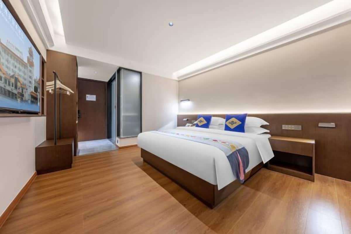Habitación de hotel con una cama grande, piso de madera, televisor y vistas a un edificio.