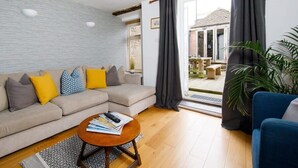 Un salon moderne avec un canapé d’angle beige, une table basse ronde et une grande fenêtre avec des rideaux.